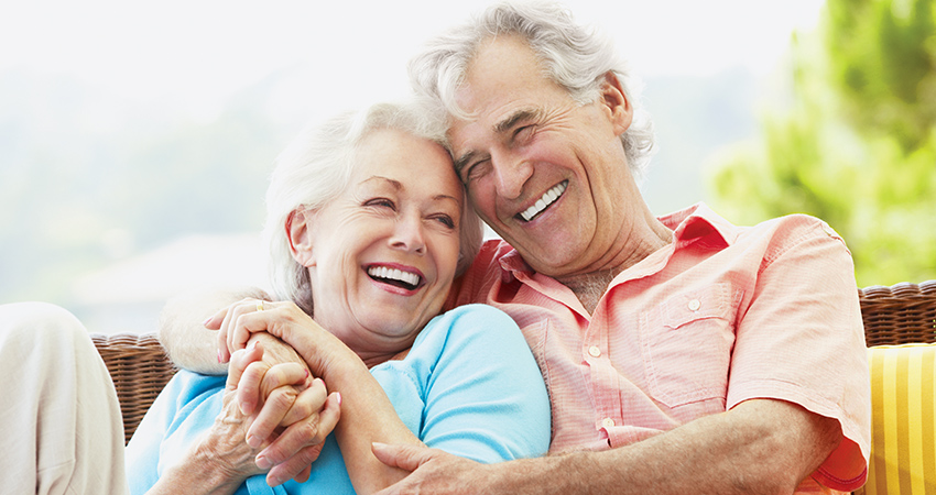 Older couple cuddle together, smiling and showing off their beautiful white dentures